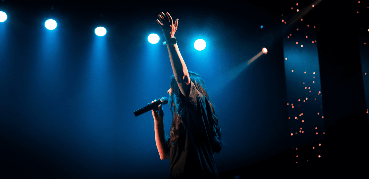 Female performer on stage holding a microphone with left arm raised